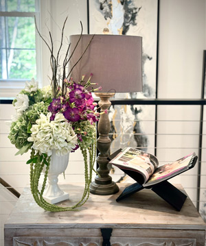 photo of floral arrangement on table with lamp & book in front of a window